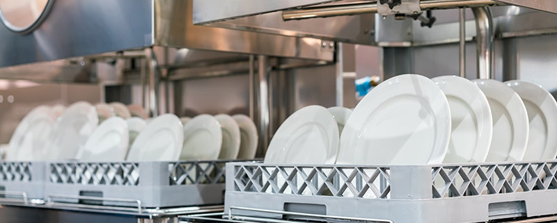 racks of plates coming out of an industrial dishwasher