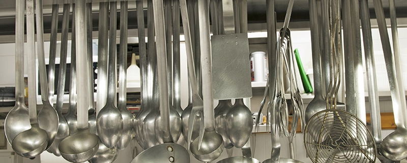 Various ladles and slotted spoons hanging from a rack in a professional kitchen